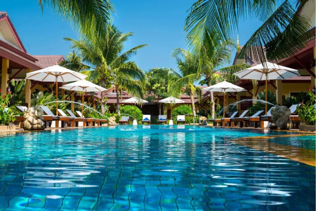 Tropical resort pool surrounded by palm trees and shaded loungers