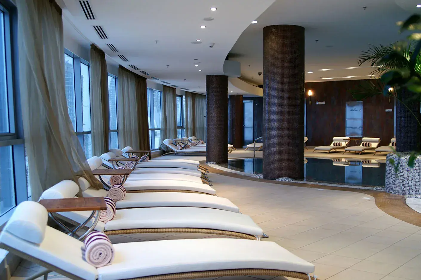 Indoor spa relaxation area with cushioned loungers beside a pool