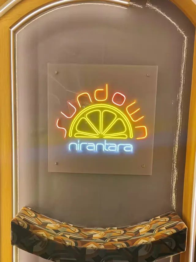 Neon Sundown sign with a citrus-slice motif mounted above a patterned bench in an arched alcove